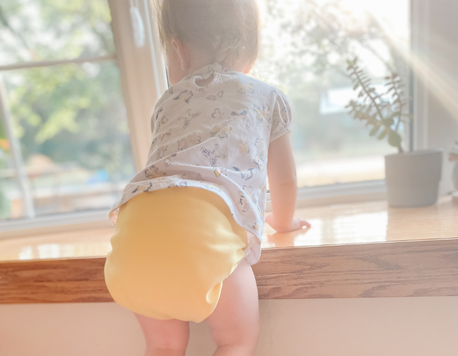 Toddler standing at a window in a bright yellow Mother-ease cloth diaper